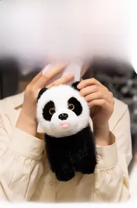 Close-up of a soft plush panda toy with fluffy fur being held by hands in a warm room