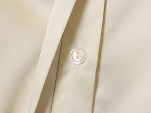 Vue macro détaillée du tissu satiné beige de la chemise avec un bouton blanc et texture fine