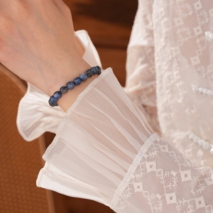 Close-up of deep blue stone bead bracelet worn with an elegant white lace cuff