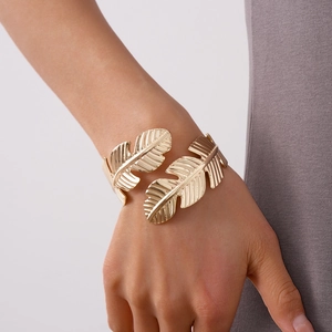 Detail of a golden feather-shaped open cuff bracelet with intricate brushed metal texture