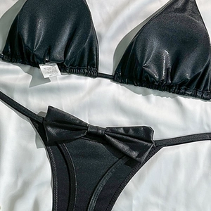 Close-up of black triangle bikini set with metallic finish and decorative bow on silk fabric