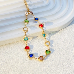 Close-up of heart-shaped colorful zircons on a gold-plated chain bracelet set on white steps