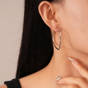 Detail of silver twisted hoop earrings with hammered texture on a female model