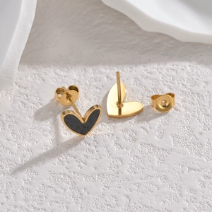 Minimalist gold heart earrings with black enamel inlay and butterfly backs on white surface