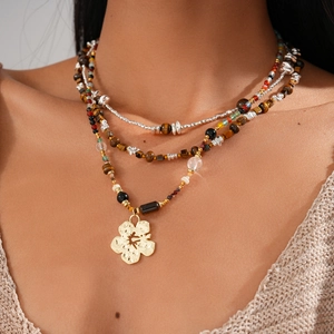 Detail of layered beaded necklace with a textured gold flower pendant in boho style