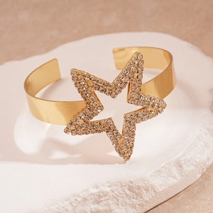 Macro shot of gold metal cuff bracelet with crystal studded star on textured stone