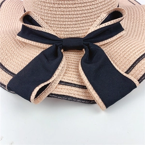 Detailed close-up view of a large black ribbon bow on a beige woven straw sun hat