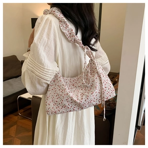Detailed view of floral underarm bag with pleated strap on a model in a cozy indoor setting