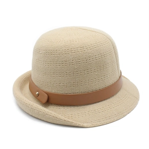 Close-up of beige knit bucket hat featuring a brown leather strap and gold rivet detail
