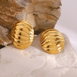 Macro view of gold-tone oval earrings with ribbed texture on natural stone surface