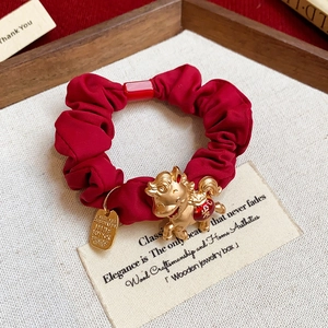 Détail d'un chouchou rouge plissé avec un pendentif dragon doré et une petite médaille