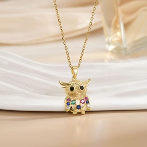Close-up of golden owl pendant with colorful gemstones and black eyes on a fine chain