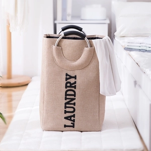 Beige laundry basket with metal handles and Laundry print in a bedroom setting
