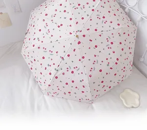 Detail of cream umbrella with red cherry print spread on a white minimalist bed