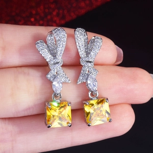 Detail of luxury radiant cut yellow gemstone bow earrings held in hand for scale