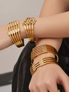 Primo piano di bracciali geometrici cavi dorati con pietre incastonate sul braccio di una modella