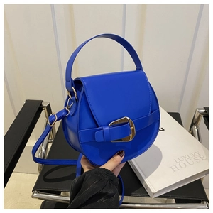 Detail der blauen PU-Satteltasche mit Goldschnalle und Griff auf einem schwarzen Stuhl