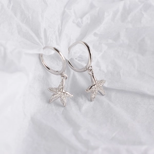Detail of silver starfish drop earrings with white zirconia stones on textured background