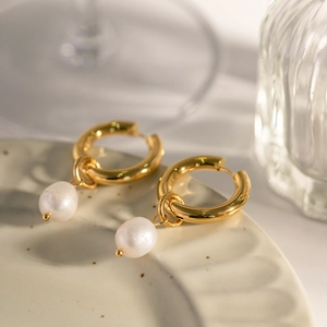 Elegant gold hoop earrings with freshwater pearl pendants on a ceramic tray