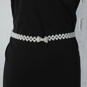 Detail view of pearl waist chain featuring a sparkling rhinestone bow buckle on a black dress