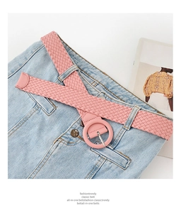 Detailed view of a pink woven PU leather belt with a matching round buckle on denim