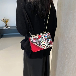 Red crossbody bag with artistic graffiti print and gold chain strap shown on model