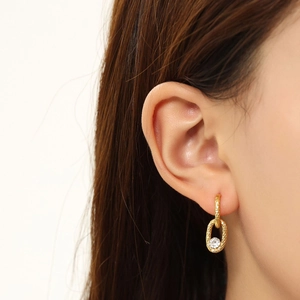 Detail of gold woven oval earring featuring a clear round crystal on ear model