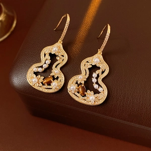 Golden gourd earrings with pearls and a brown gemstone on a leather jewelry box