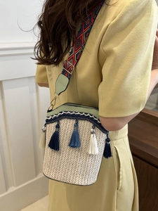 Detail of beige woven straw bucket bag with colorful geometric strap and tassel charms