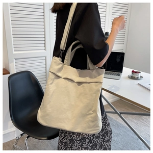 Detail view of a large cream nylon tote bag worn by a model in a modern office setting