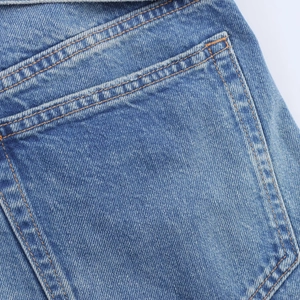 Détail du short en jean bleu montrant les coutures orange et la texture de la poche arrière