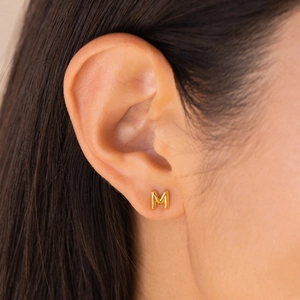 Minimalist gold titanium steel stud earring in M-letter shape shown on model's ear
