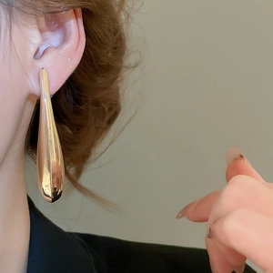 Close-up of oversized teardrop golden earrings with a polished mirror finish on a model