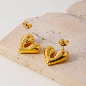 Polished golden 3D heart stud earrings made of stainless steel on natural stone background