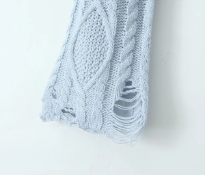 Detail of light blue cable knit sweater featuring intricate patterns and frayed hem