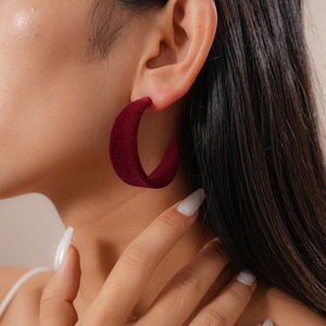 Close-up of deep red velvet C-shaped earring worn by a model in a minimalist style