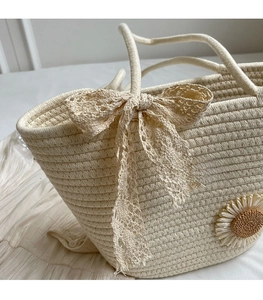 Detail of hand-woven tote bag featuring a cream lace bow and sunflower applique