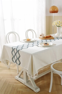 Detail of beige linen table runner with blue geometric patterns and fringed edges