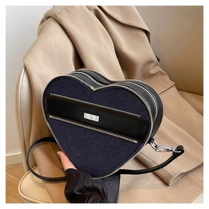 Detail of heart-shaped denim crossbody bag with black leather trim on a light blazer