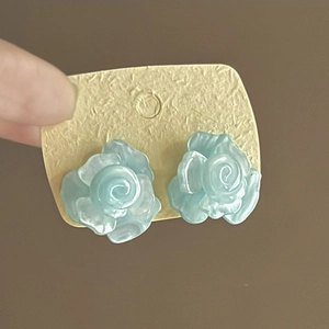 Close-up of light blue resin rose flower earrings displayed on a cream jewelry card