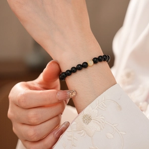 Detail of obsidian beaded bracelet with yellow amber bead on an embroidered sleeve