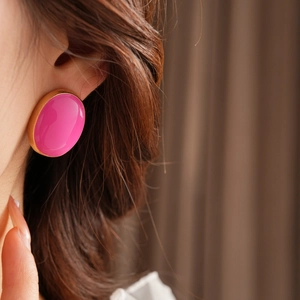 Close-up of a vintage oval magenta enamel earring with gold border worn by a model