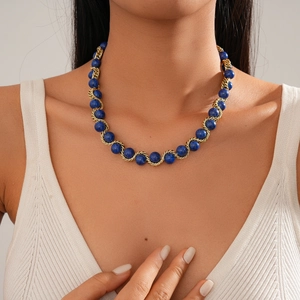 Elegante collana a catena dorata con perle blu indossata da una modella su sfondo neutro
