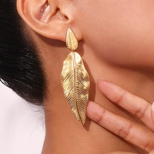 Close-up of a large gold leaf earring on a model showing the metallic texture and size