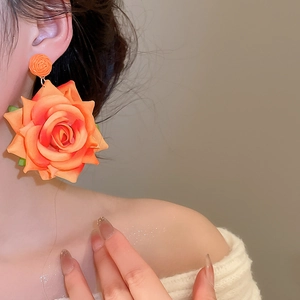 Detailed view of orange fabric rose earrings worn by a model for a sweet resort look