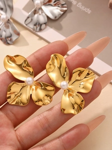 Detail der goldenen Blütenohrringe mit weißer Perle und metallisch gewelltem Design