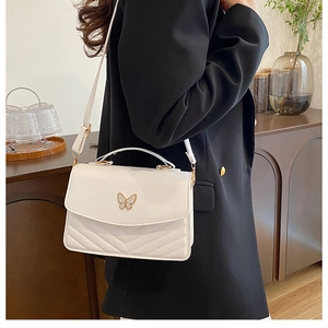 Detail of white quilted crossbody bag with metal butterfly clasp on a side-view model