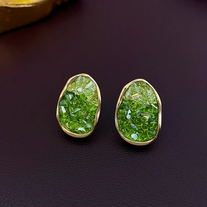 Detail of irregular gold earrings with faceted green crystals on brown leather texture