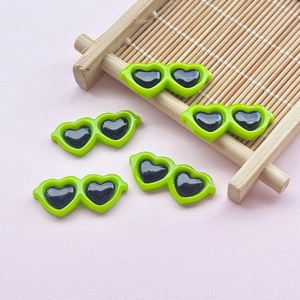 Macro shot of five green resin heart-shaped mini sunglasses for DIY crafts on pink background