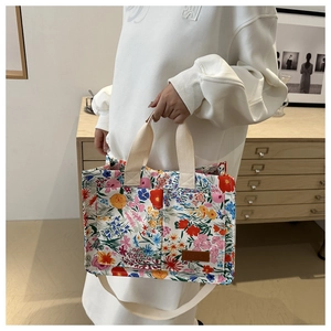 Detail showing the floral canvas tote bag with brown leather patch and woven handles
